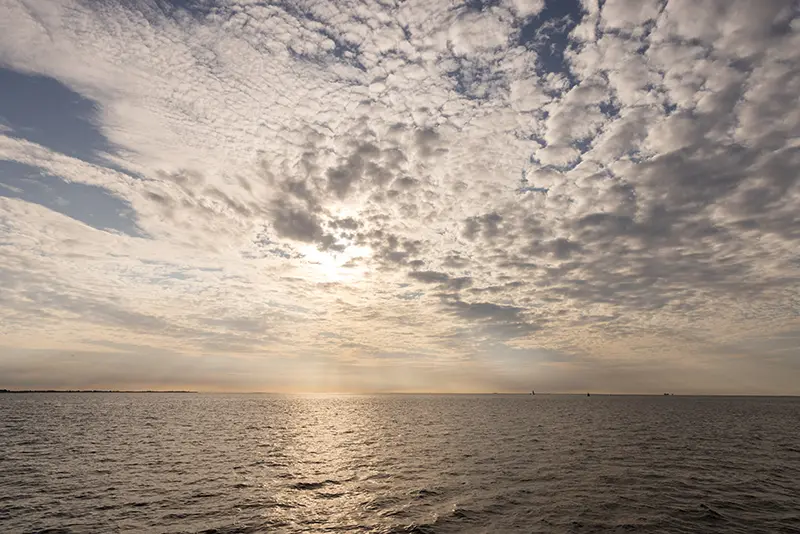 zee en wadden met zon achter licht wolkendek